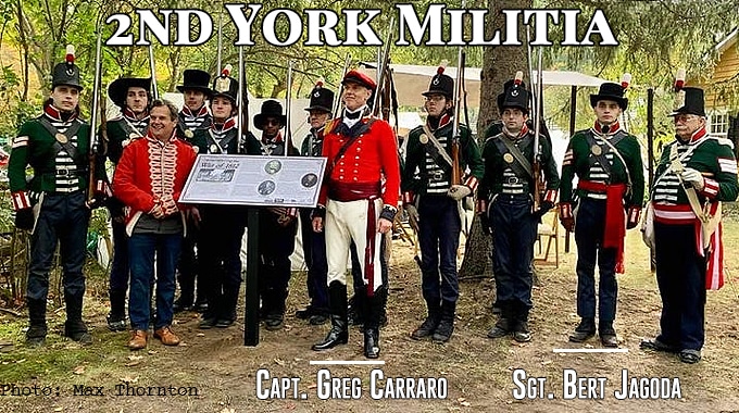The 2nd York Militia in green and red uniforms with muskets, standing in a line outdoors; Capt. Greg Carraro and Sgt. Bert Jagoda are labelled